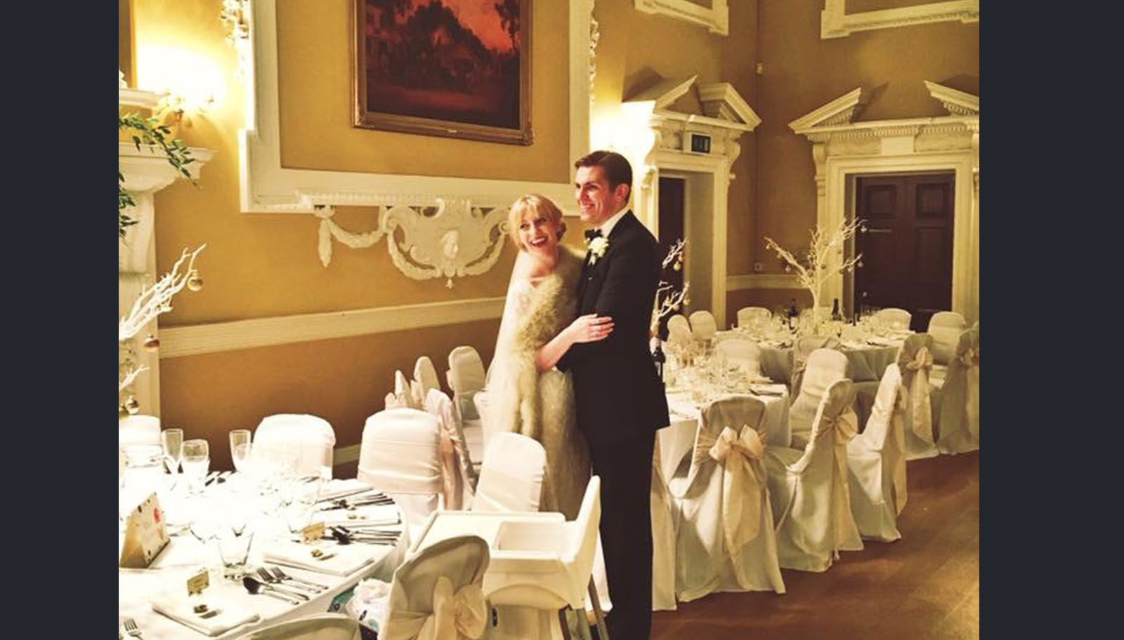 A Newlywed couple posing at their reception in the Ball Room of Bedale Hall. 